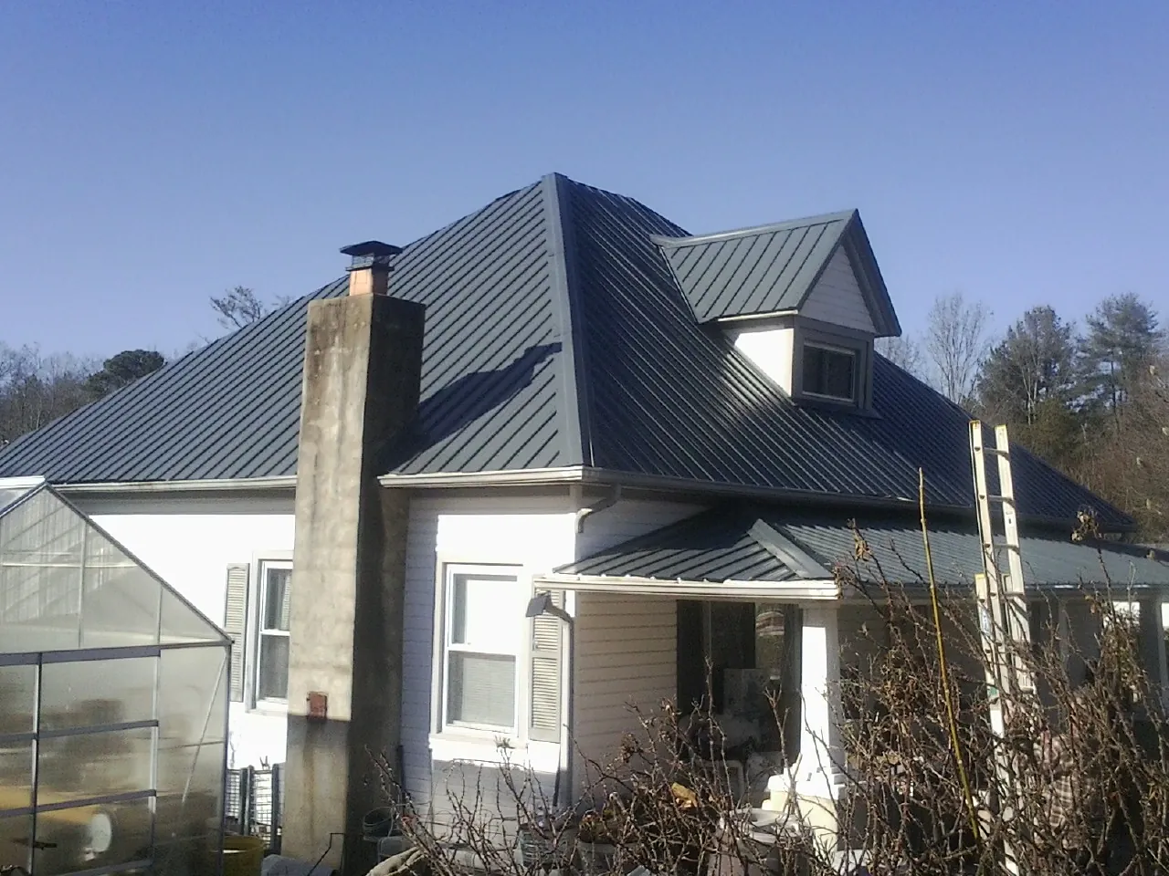 Dark blue standing seam metal roof on a white farmhouse with dormer — Slate & Tile Roof Repair by Roofing Brothers in Cyril