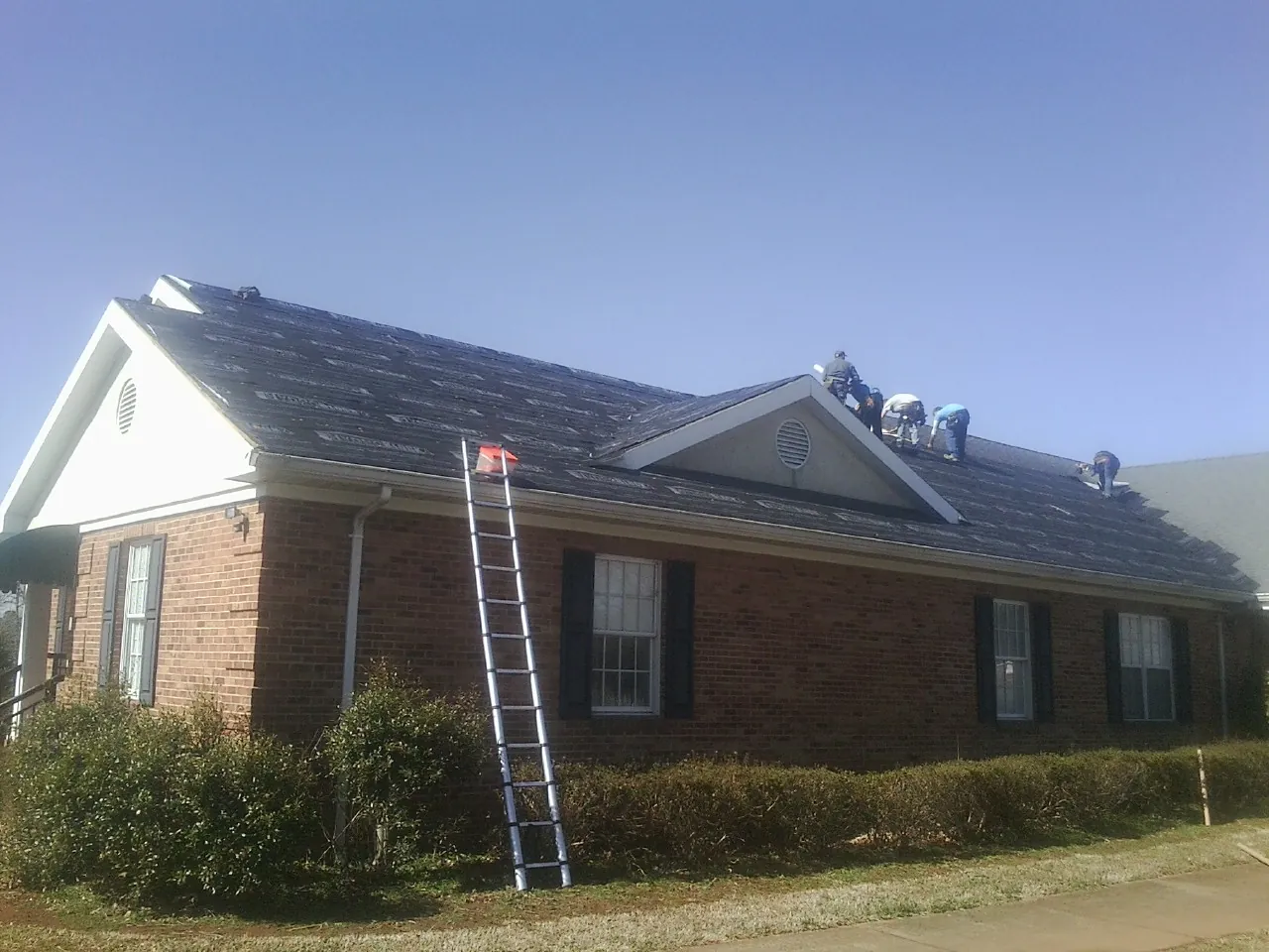 Crew tearing shingles off a brick ranch roof with a ladder set — Emergency Roof Repair work by our crew in Cyril