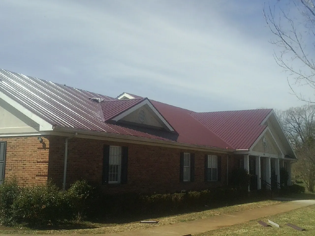 Red metal roof with gabled entries on a long brick building, from a Hail Damage Roof Repair job in Cyril
