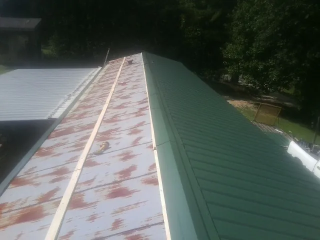 Old rusted panels beside newly installed green metal roofing — Wind Damage Roof Repair by Roofing Brothers in Cyril