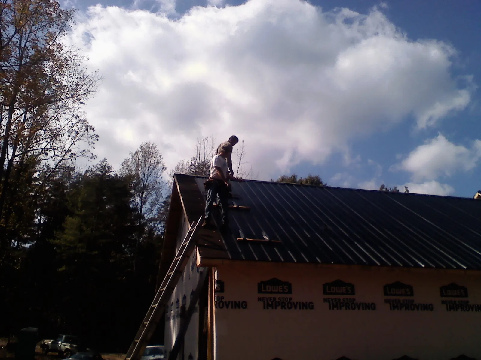 Roofer fastening dark metal panels high against a cloudy sky, from a Roof Inspection job in Cyril