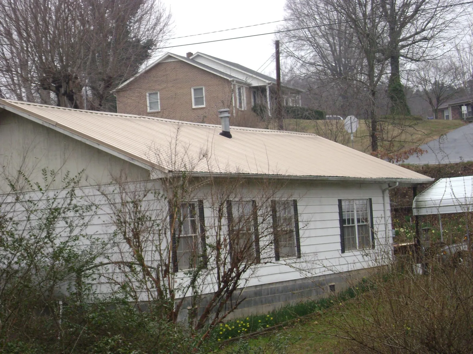 Tan metal roof on a white sided house set into a hillside — Commercial Roofing by Roofing Brothers in Cyril