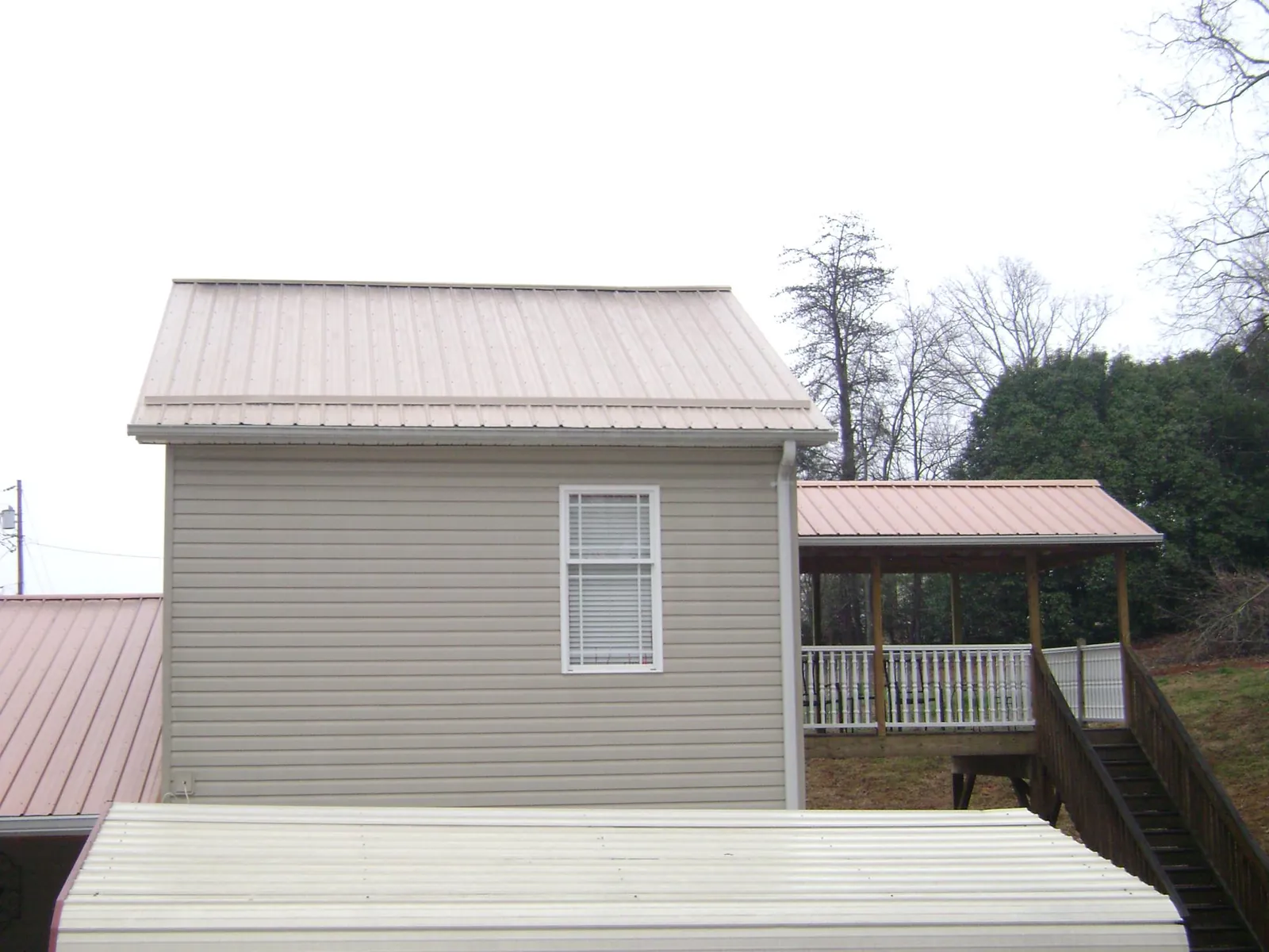 Tan metal roofs on a two story addition and attached porch, from a Roof Replacement job in Cyril